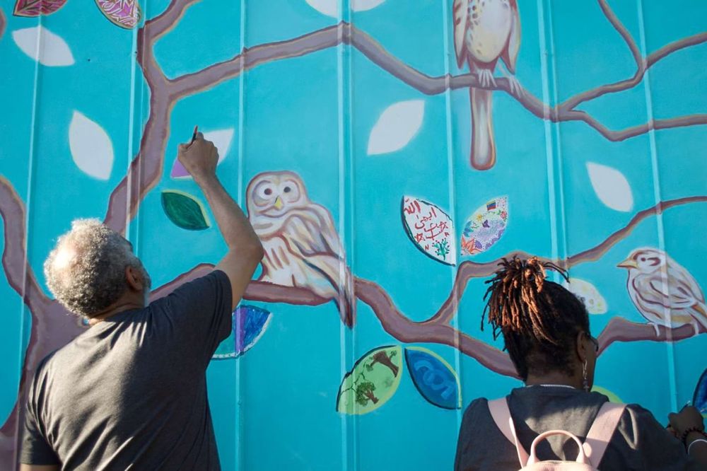Two individuals paint a mural on a water tower as part of a service project.
